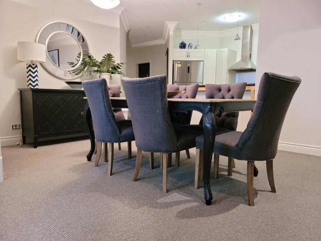Un comedor con una mesa redonda, cuatro sillas, un espejo, una lámpara y una planta en maceta.