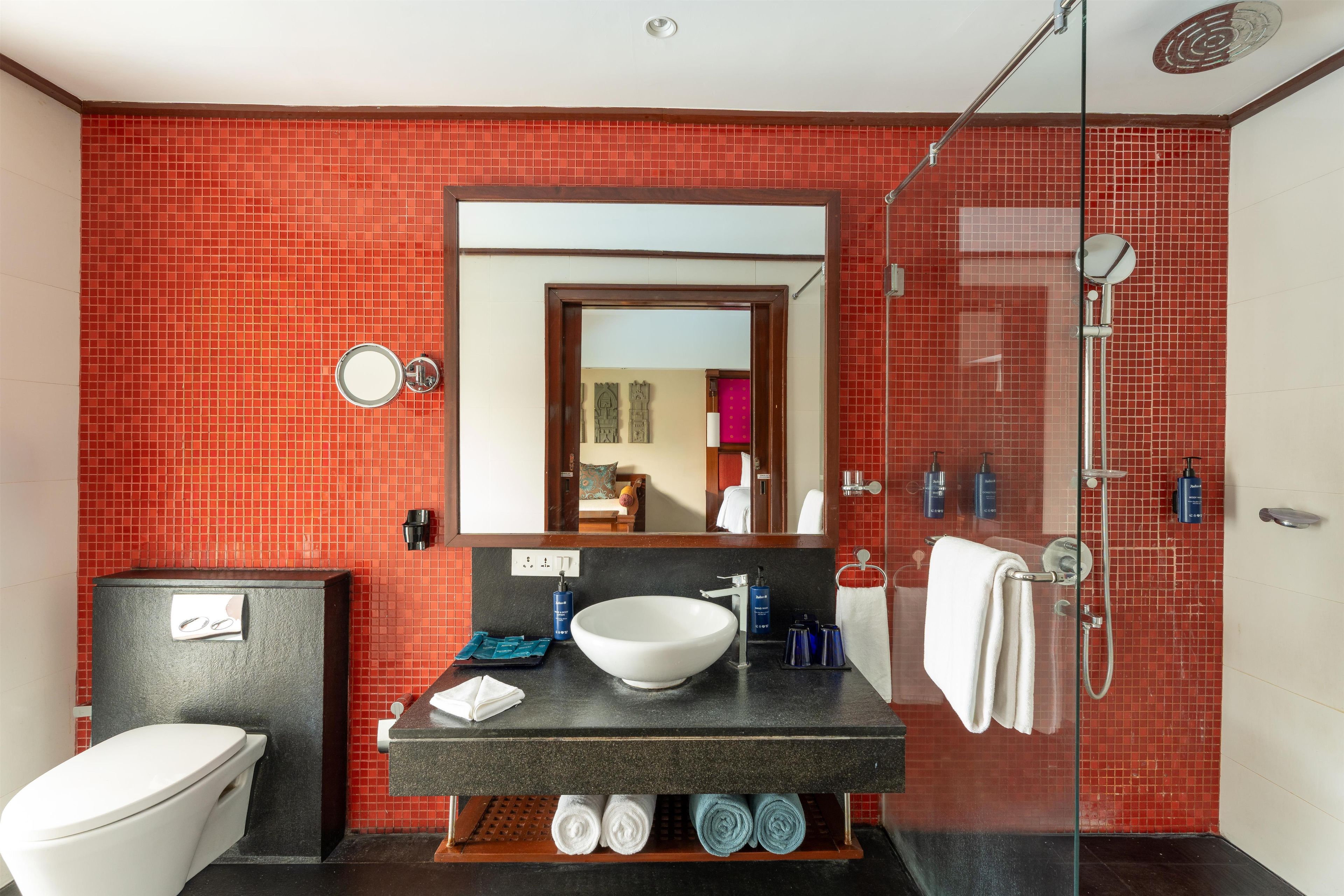 A modern bathroom with a large mirror, a white sink, a glass shower enclosure, and a toilet.