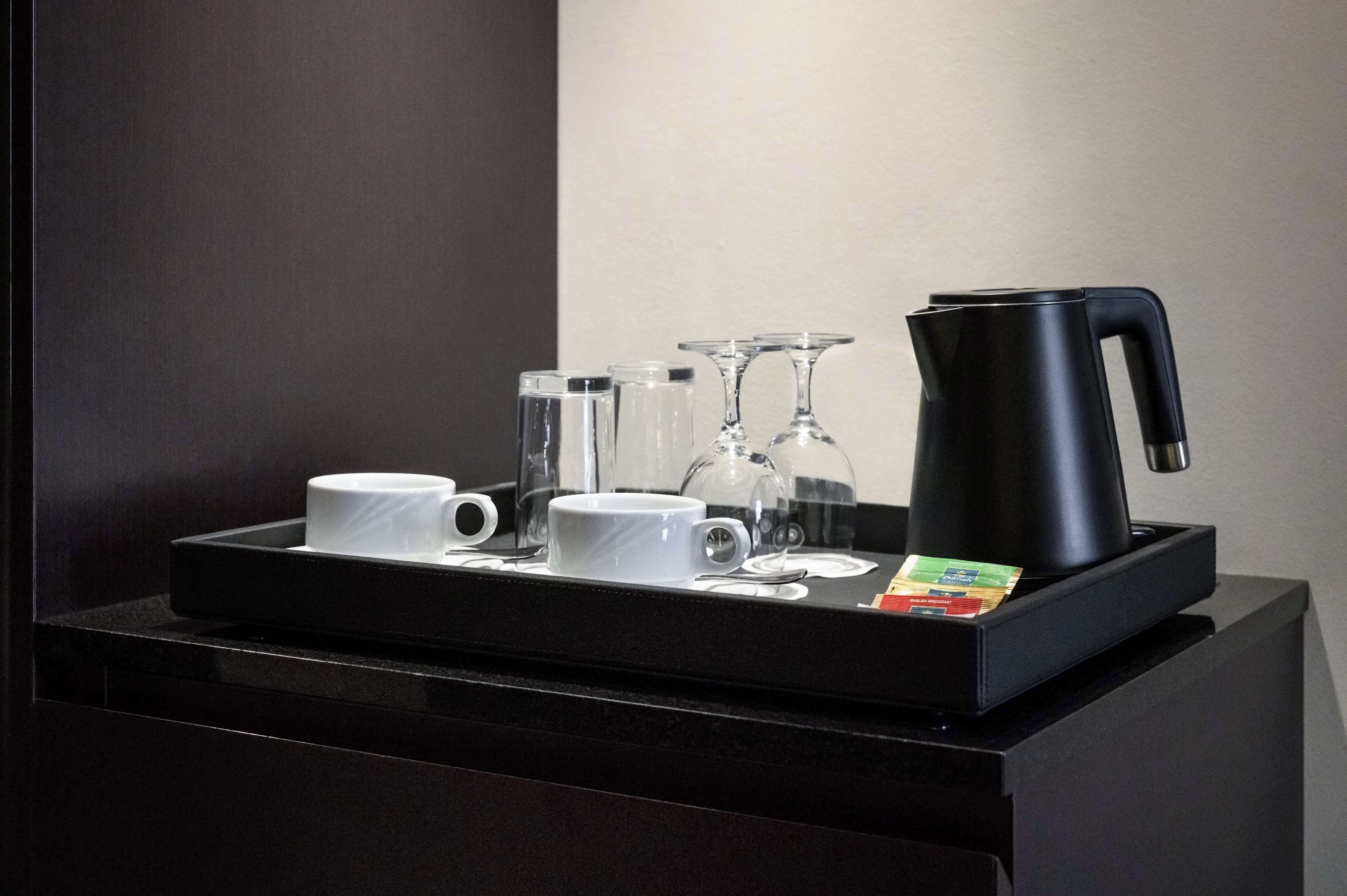 Una bandeja negra con una cafetera, dos tazas blancas, dos vasos de vidrio y un sobre de azúcar.