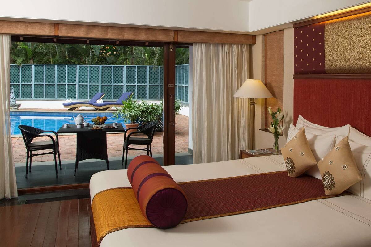 Une chambre d’hôtel avec un lit, une vue sur la piscine et un coin repas comprenant des chaises et une table.