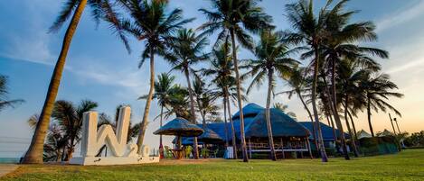 A tropical resort with palm trees, a large 'W' sign, and thatched-roof structures.