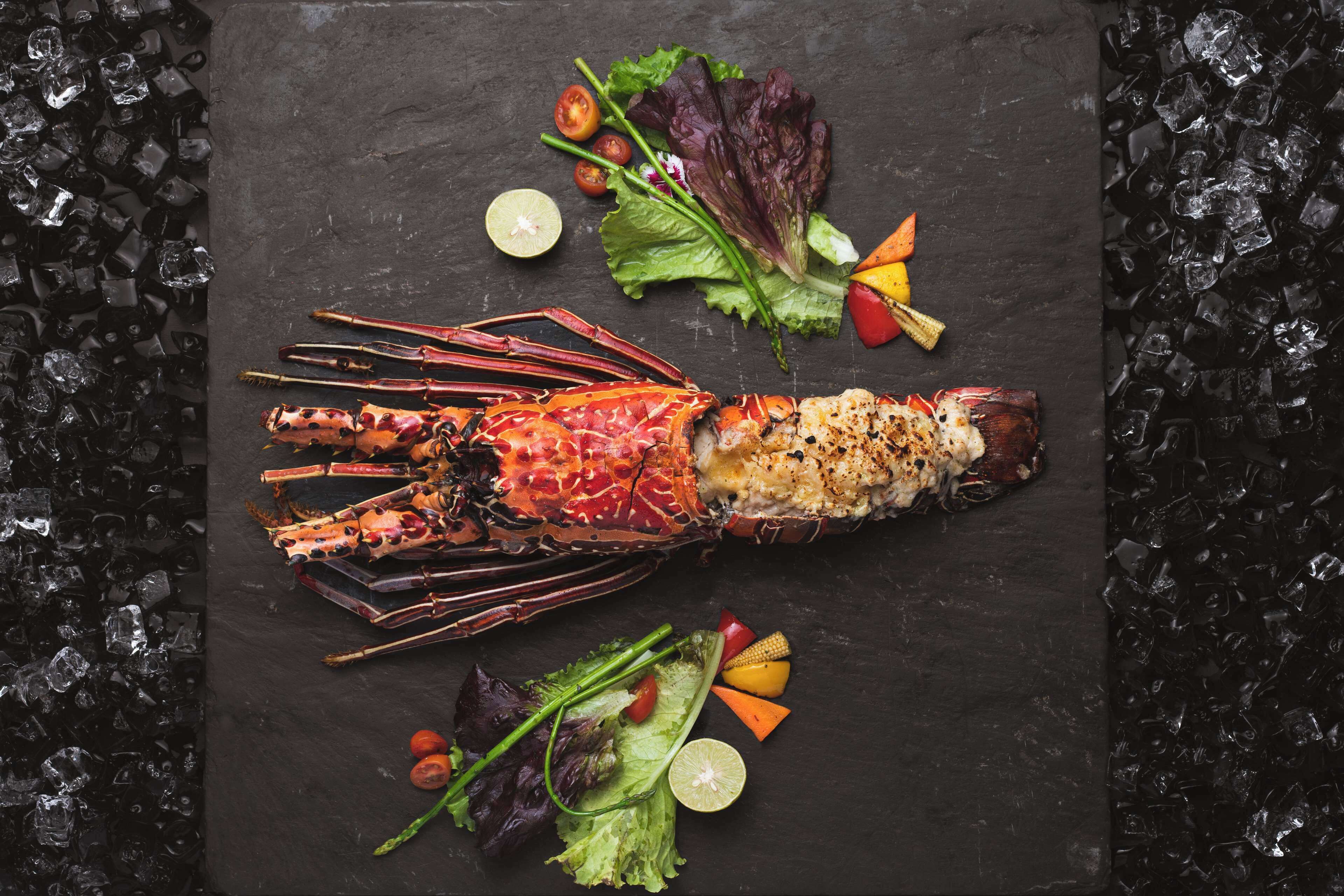 A lobster on a slate board with garnishes and ice.