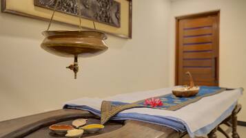 A traditional massage table with a blue cloth, a hanging brass oil lamp, and small bowls of oil and herbs.