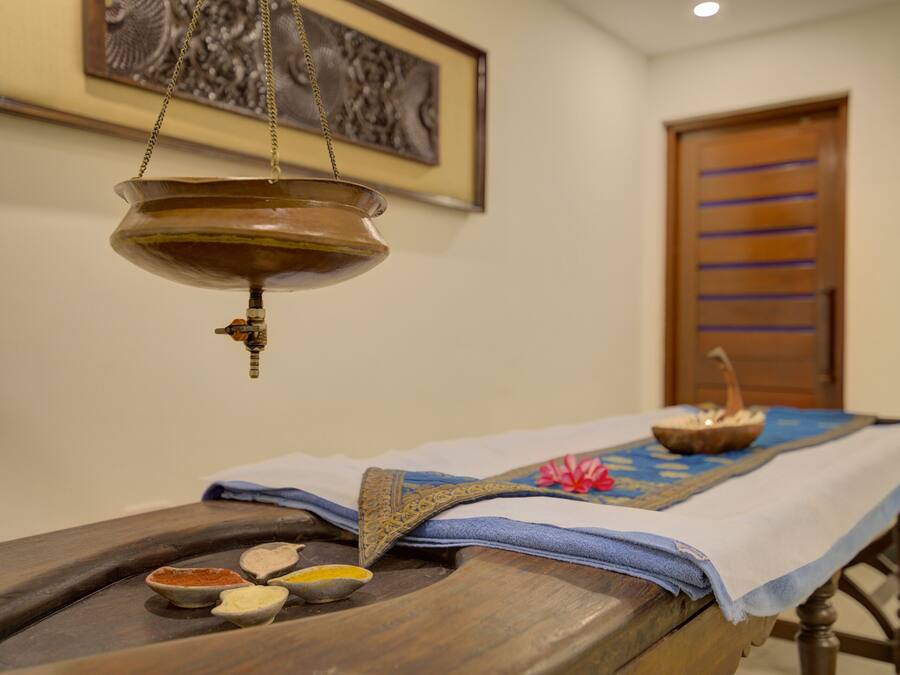 A traditional massage table with a blue cloth, a hanging brass oil lamp, and small bowls of oil and herbs.