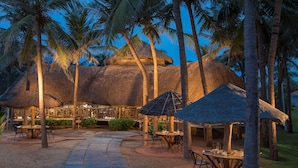 Ein Resort mit strohgedeckten Hütten, Palmen und Essbereichen im Freien.