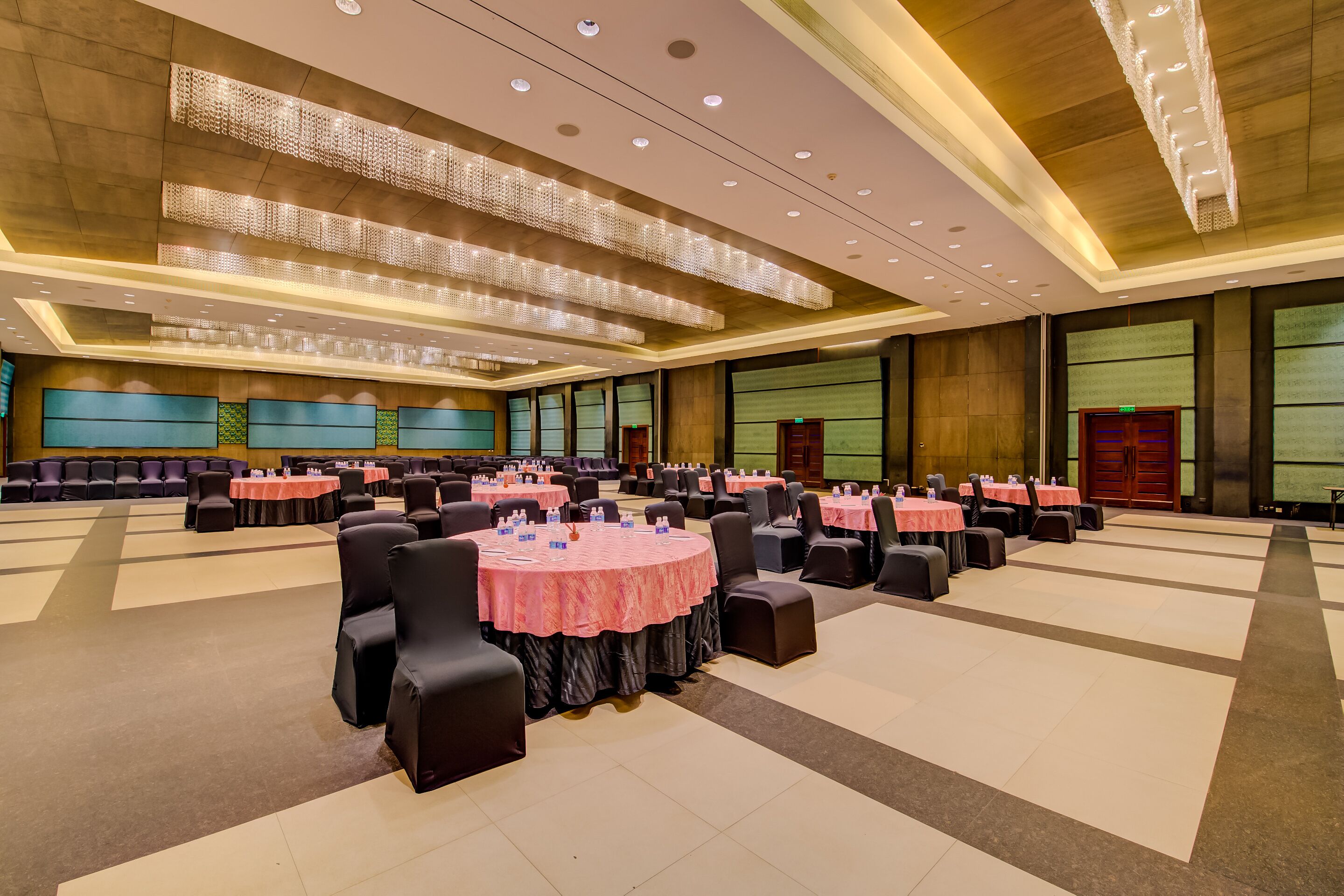 A large conference room with multiple round tables covered with pink tablecloths, arranged in rows.