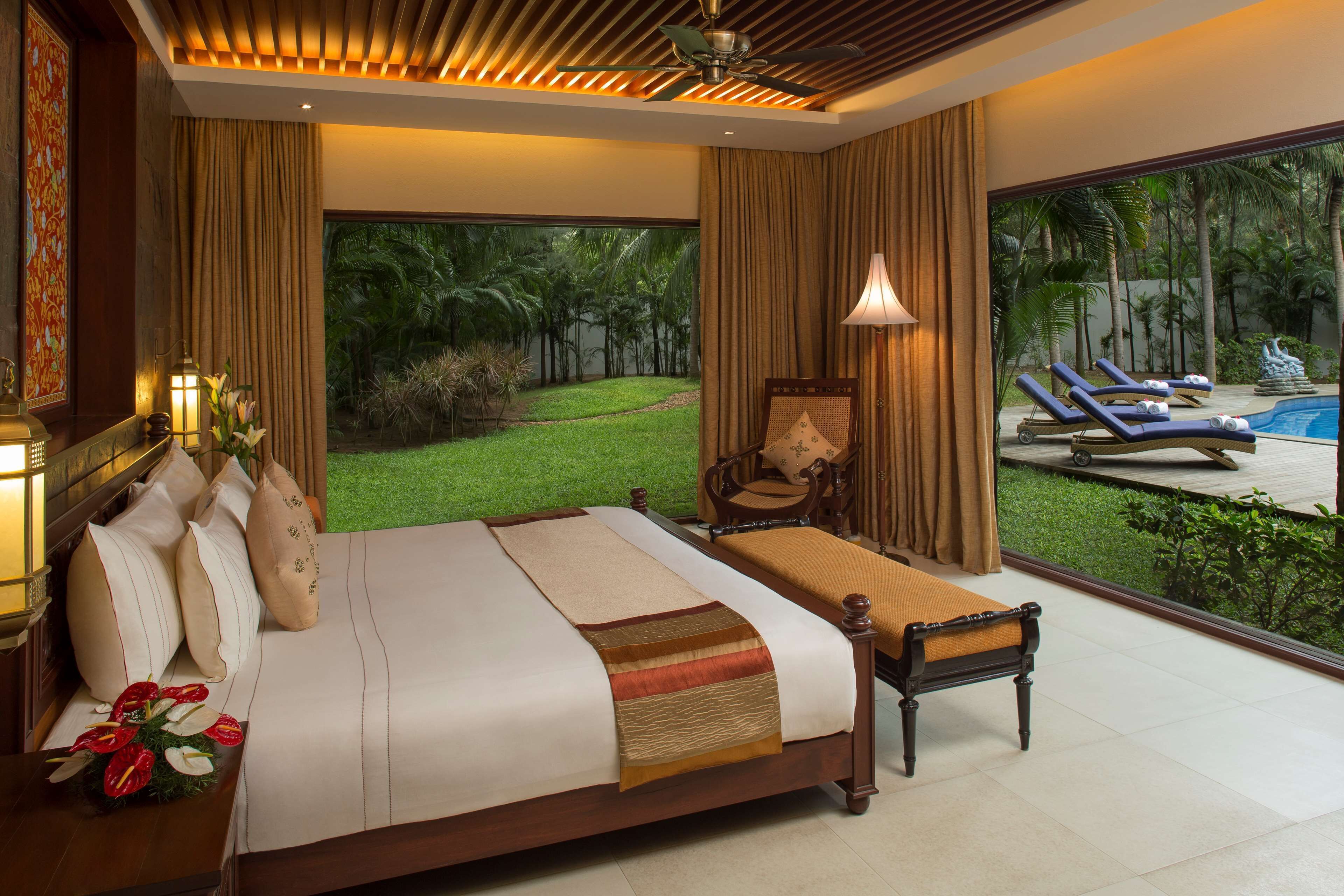 Une chambre spacieuse dotée d’un grand lit, d’un coin salon et offrant une vue sur une piscine et un jardin tropical.