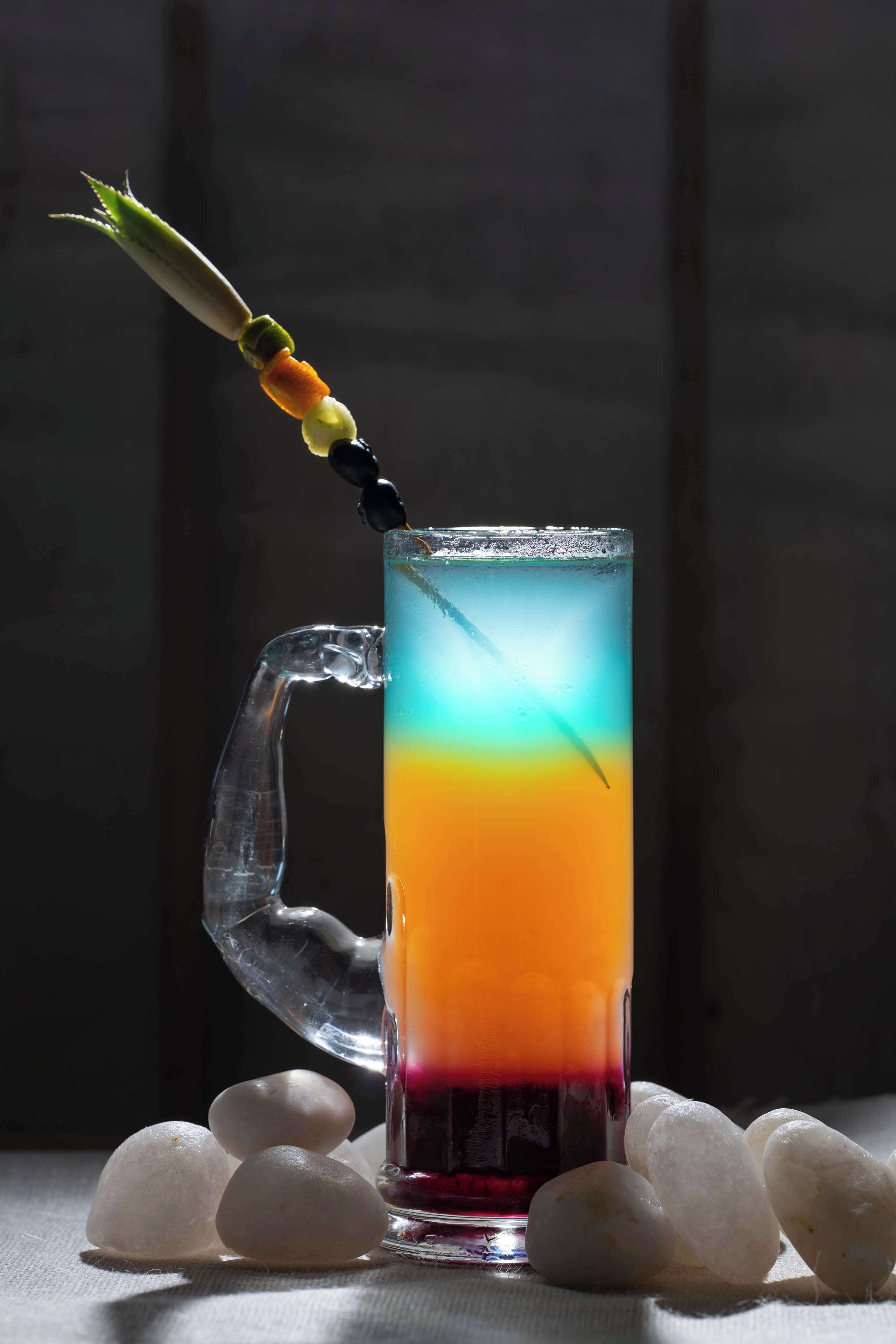 Un vaso alto con una bebida degradada, un removedor de cóctel y cubitos de hielo sobre una mesa.