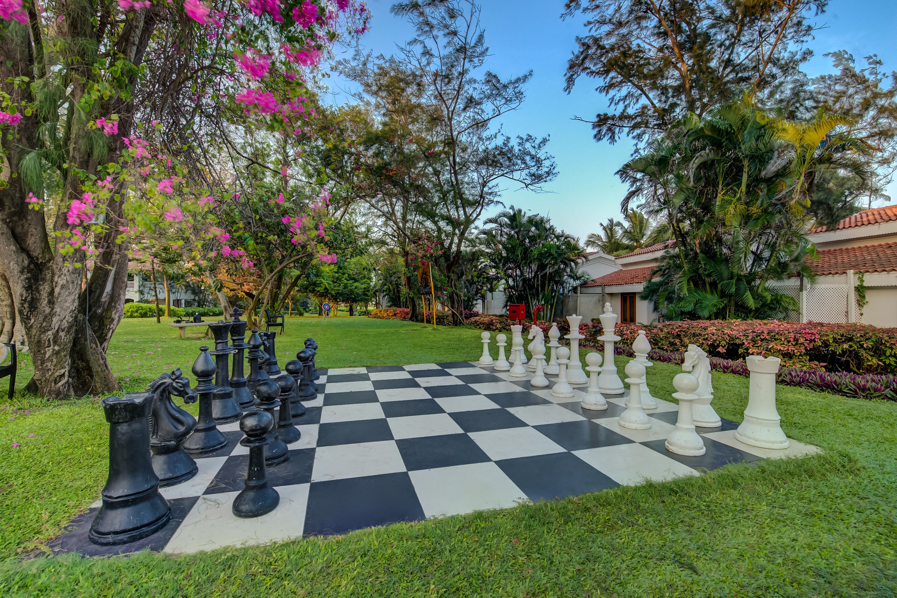 A large outdoor chessboard with chess pieces set up in a garden area.