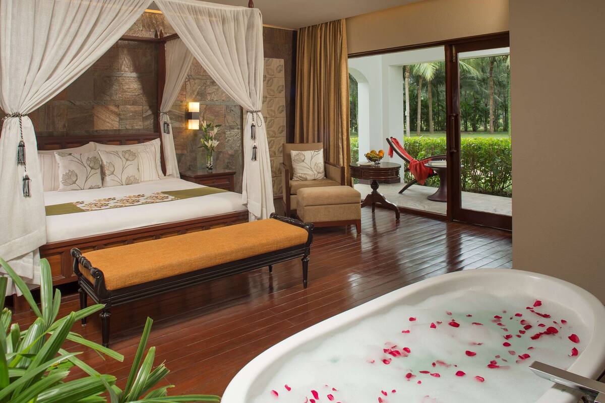 Une chambre dotée d’un grand lit, d’un coin salon avec un fauteuil et une table, et d’une salle de bain avec une baignoire.
