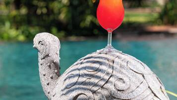 Une statue de tortue en pierre, avec un verre d’une boisson rouge et une cerise sur le dessus, placée près d’une piscine.