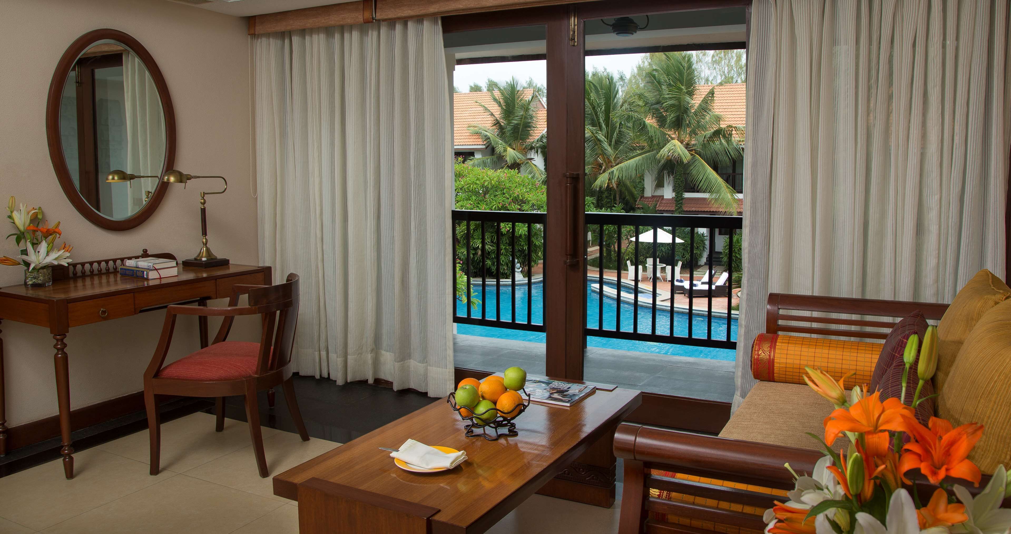A hotel room with a desk, chair, and a view of a swimming pool and palm trees.