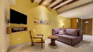 A modern living room with a yellow wall, a flat-screen TV mounted on the wall, a wooden chair, a round wooden table, and a purple sofa.