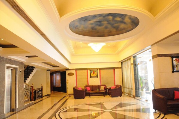 A spacious lobby with a central seating area, a staircase, and a large chandelier.