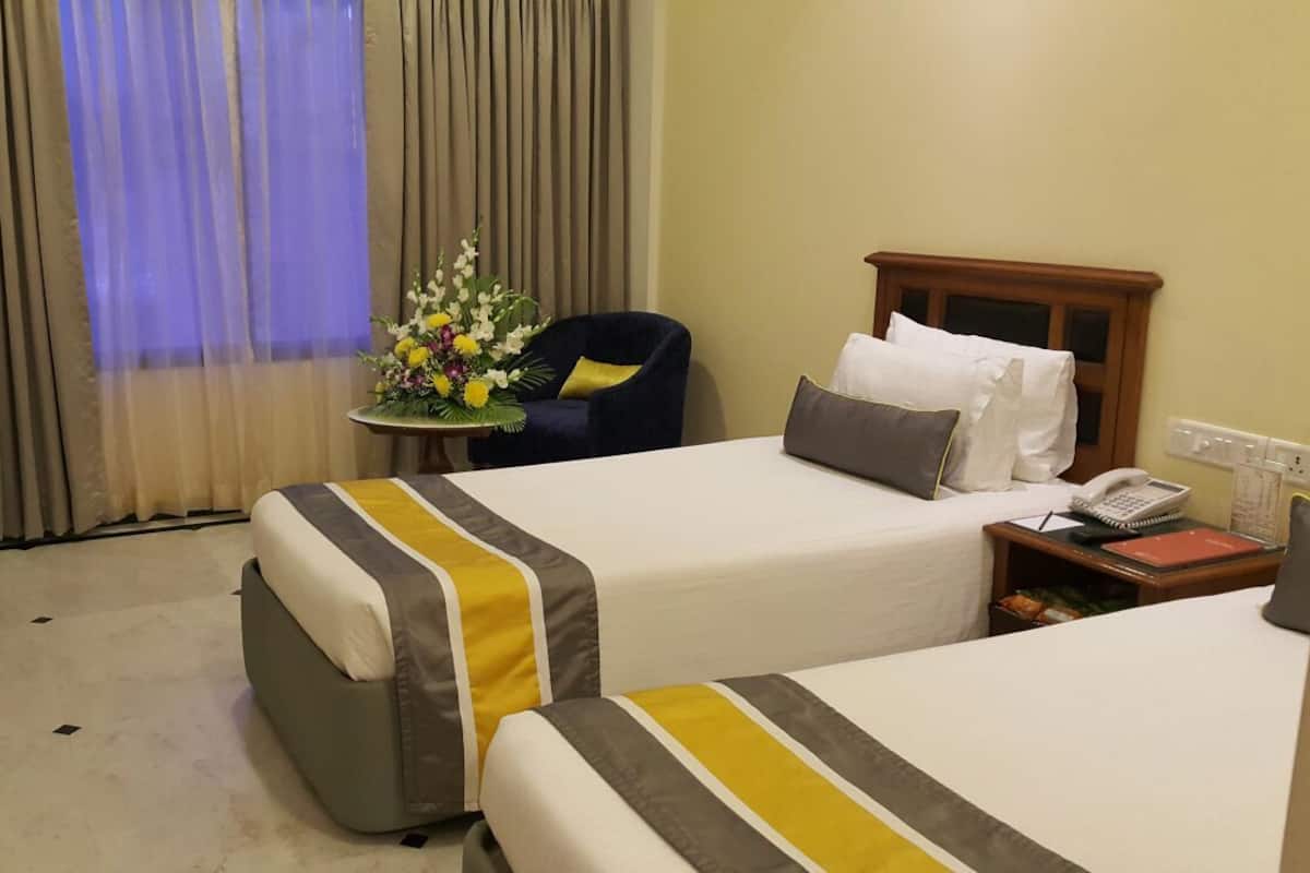 A hotel room with two beds, a desk, a chair, a small table with a vase of flowers, and a nightstand with a phone and a lamp.