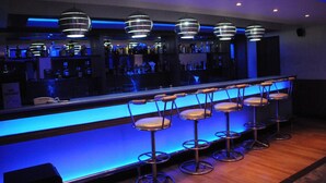 Een bar met een blauw verlichte toonbank en meerdere krukken.
