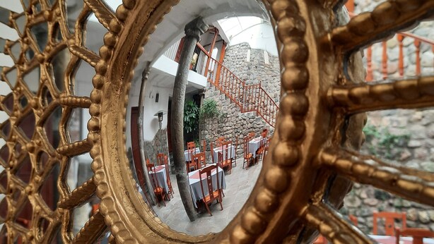 A decorative mirror with a geometric pattern, reflecting a stone wall and outdoor seating area. - Sueños del Inka Hotel (Cusco)