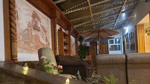 A cozy living area with a stone ledge, a large wall mural, a wooden bookshelf, and a comfortable sofa. - Sueños del Inka Hotel (Cusco)