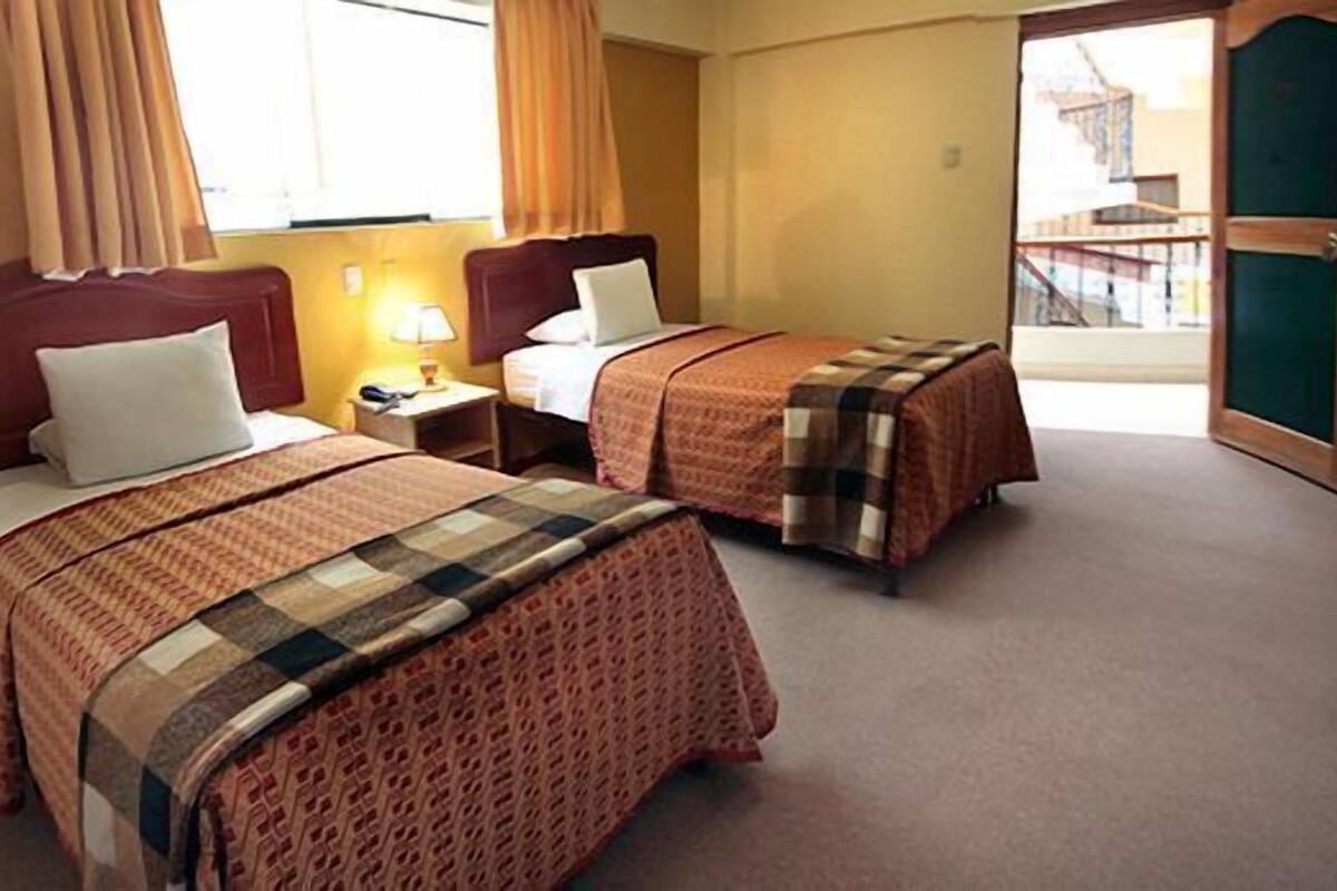 Une chambre d’hôtel avec deux lits, une table de chevet, une lampe et une vue sur un bâtiment à l’extérieur.