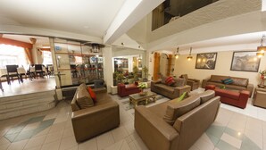 A spacious living area with multiple sofas and a coffee table, a dining area with chairs and tables, and a kitchen visible through a glass partition. - Hotel De La Villa Hermoza (Cusco)