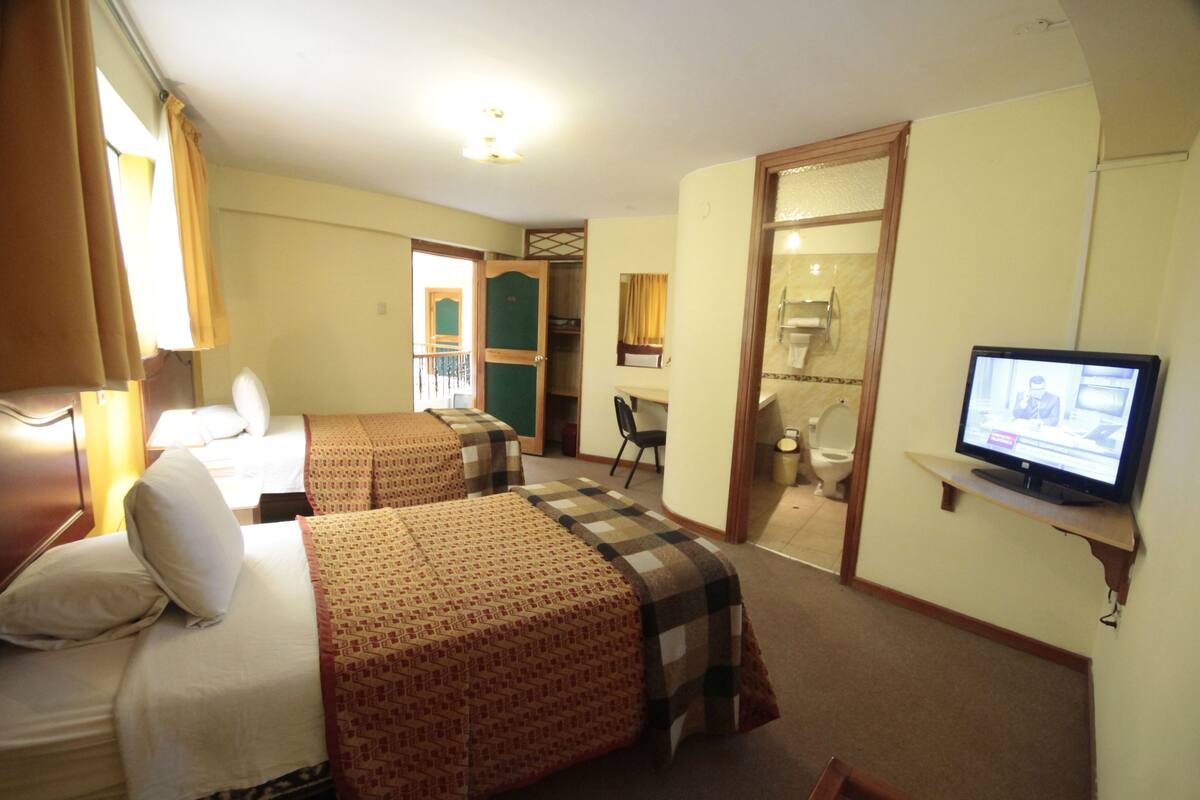 Une chambre d’hôtel avec deux lits, une télévision, un bureau et une salle de bain visible à travers une porte ouverte.