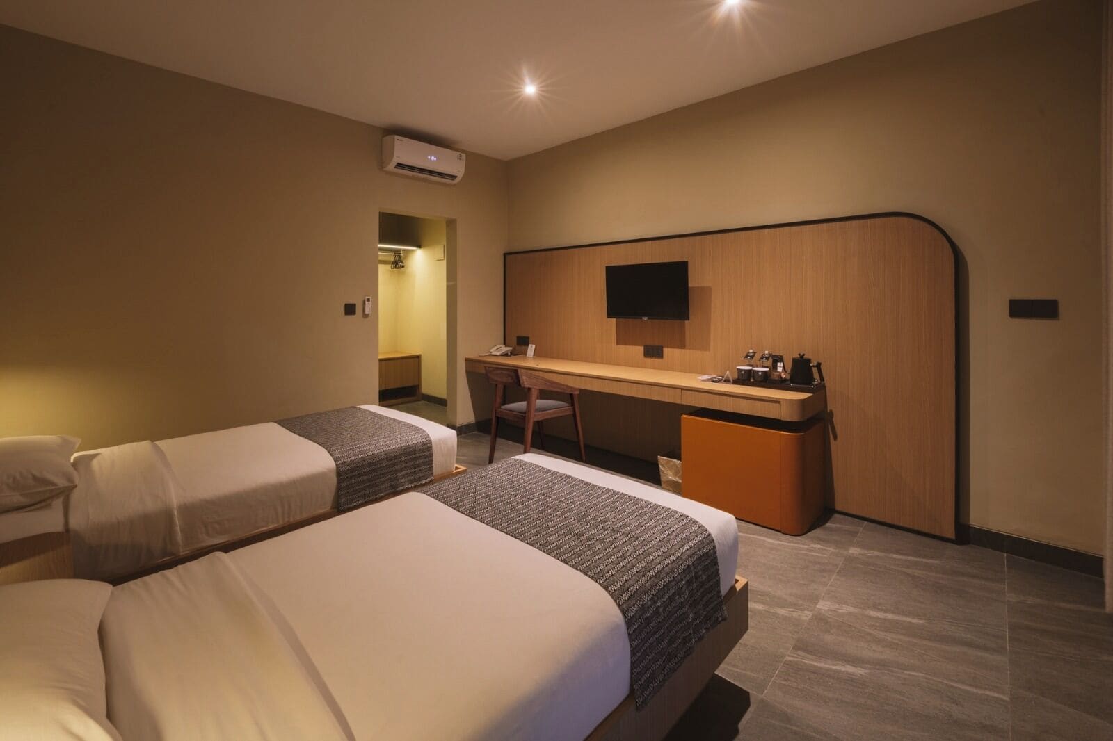 Quarto de hotel com duas camas, uma escrivaninha, uma cadeira, uma televisão e um aparelho de ar condicionado.