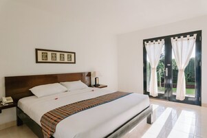 Una habitación de hotel con una cama grande, un teléfono en la mesita de noche, una lámpara y vistas a través de un ventanal.