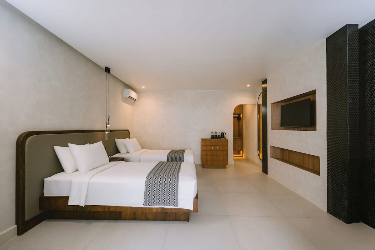 A modern hotel room with two beds, a wooden cabinet, a television, and a hallway leading to a bathroom.