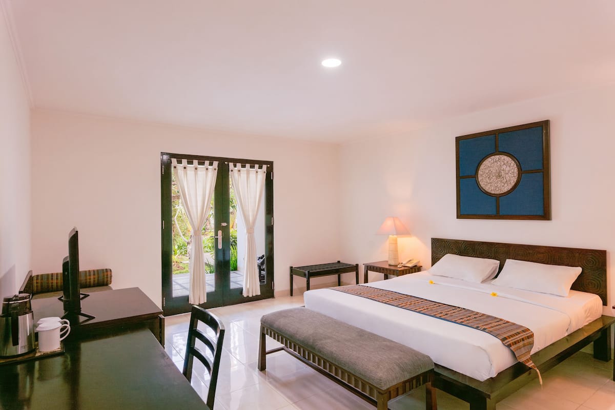 A hotel room with a bed, a desk, a chair, a laptop, a lamp, and a view of the outdoors.