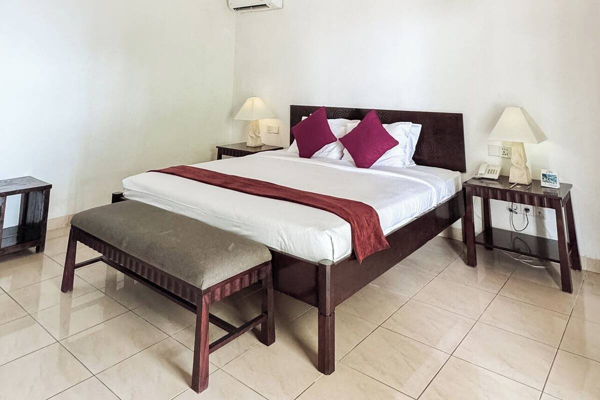 A bedroom with a wooden ceiling, a bed with a red and white bedspread, two bedside tables with lamps, and a small bench.