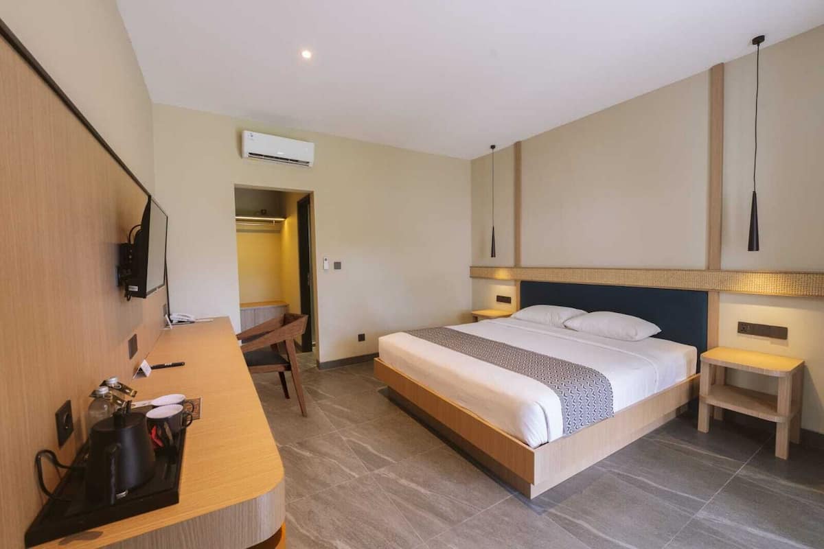 Habitación de hotel con cama, mesitas de noche, escritorio con silla, aire acondicionado y televisor.