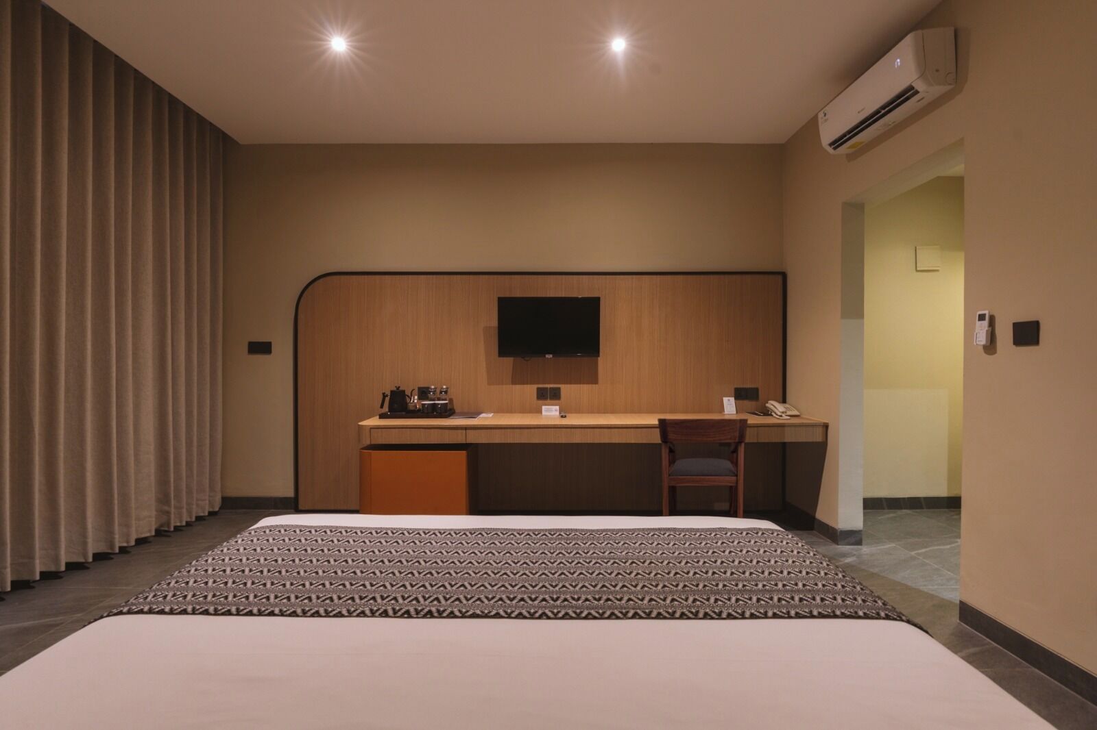 A hotel room with a bed, a desk, a chair, a flat-screen TV, an air conditioner, and a telephone.