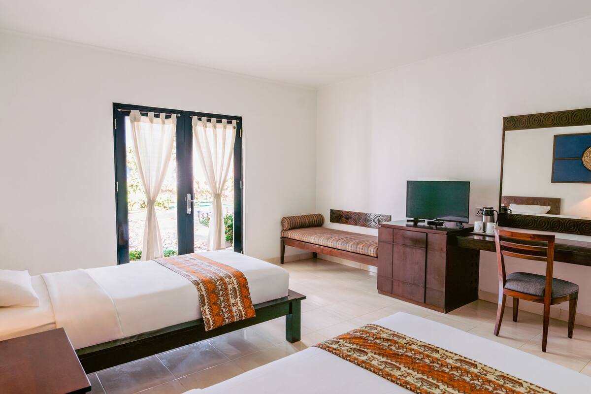 A hotel room with a bed, a desk with a chair, a television, and a window with curtains.
