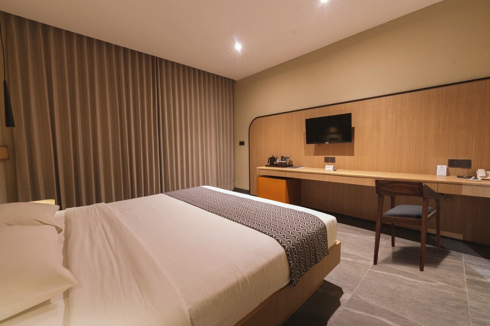A hotel room with a bed, a desk, a chair, a TV, and a curtain.