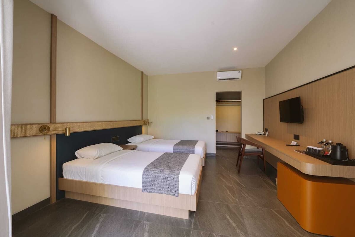 A hotel room with two beds, a desk, a TV, and an air conditioning unit.