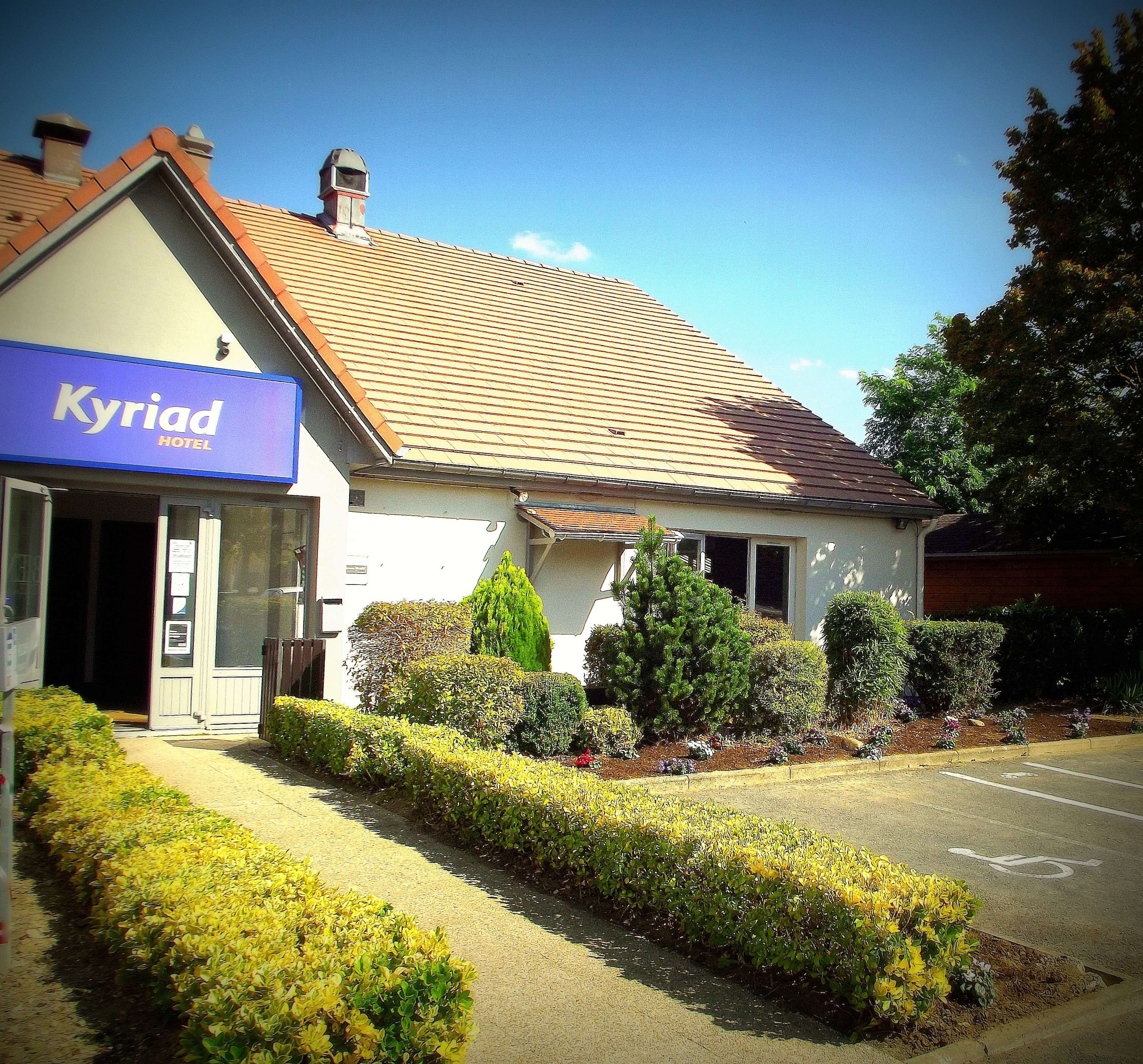 A hotel with a blue sign, a sloped roof, and a well-maintained garden.