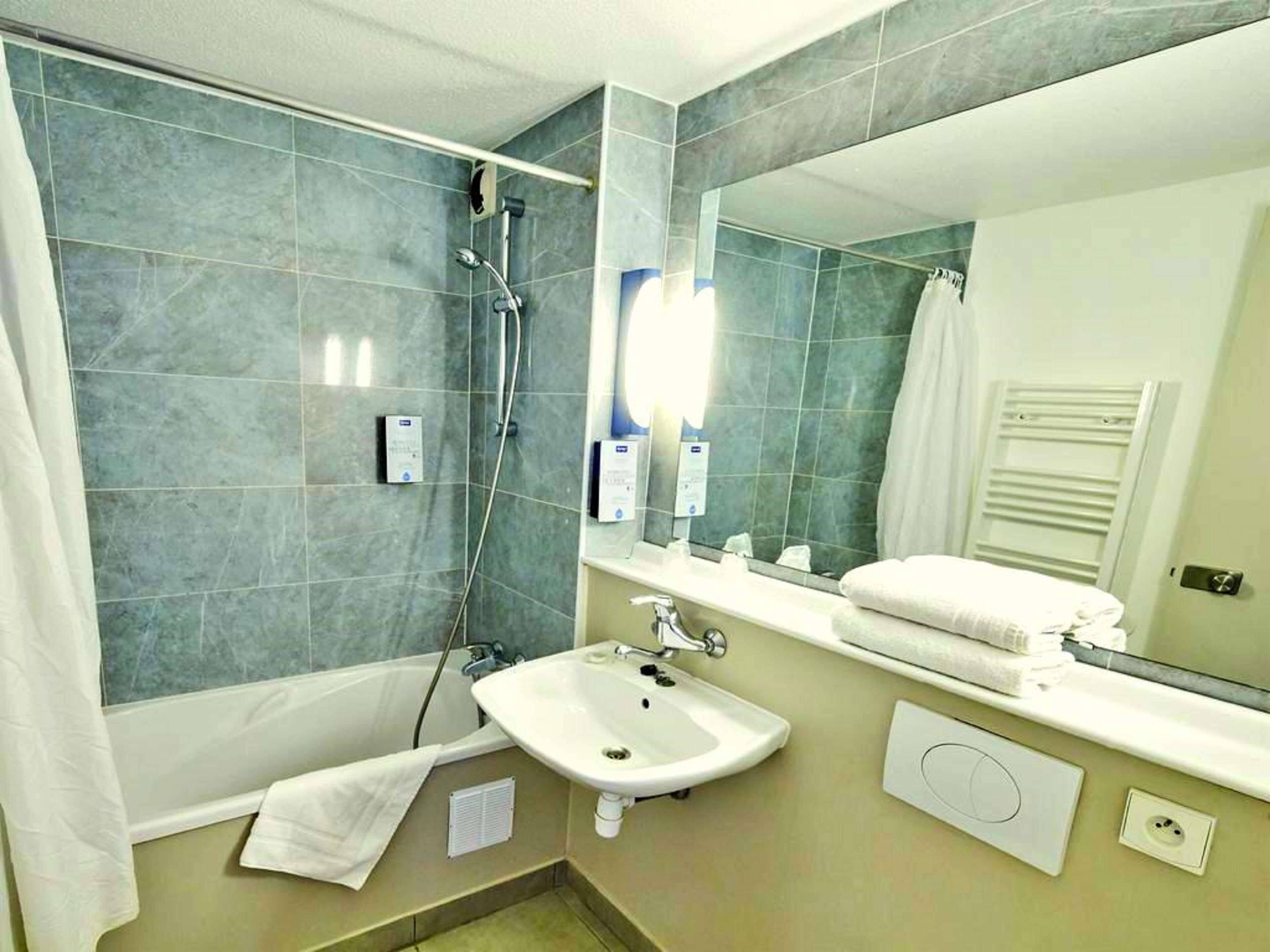 Un baño con bañera, lavamanos, espejo y perchero para toallas.