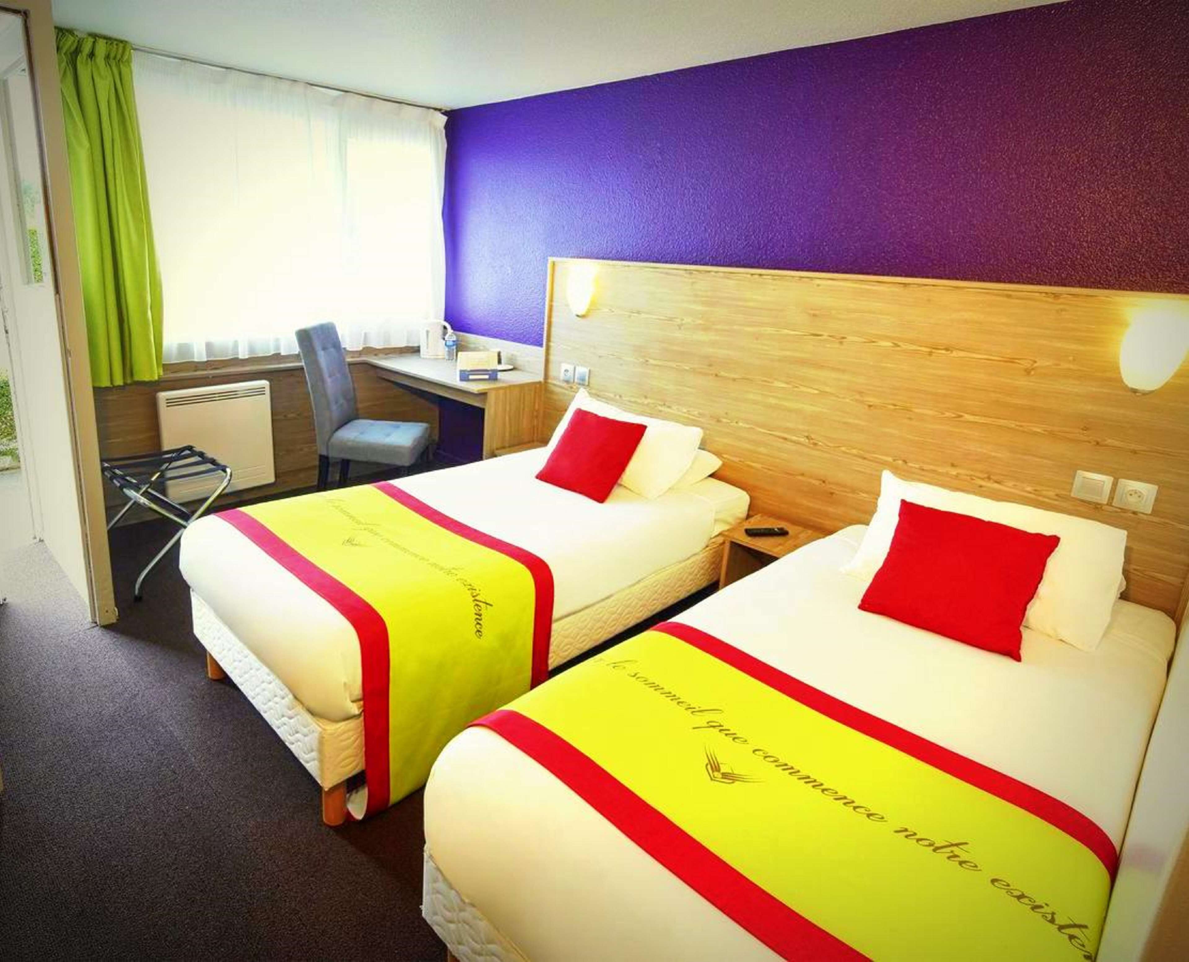 A hotel room with two beds, a desk, and a chair.
