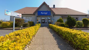 Un hotel llamado Kyriad con recepción, tejado de baldosas y un sendero bordeado por setos amarillos y verdes.