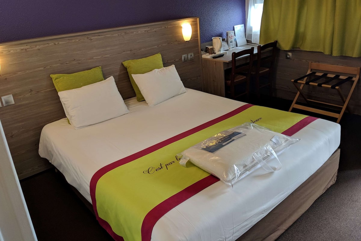 Quarto de hotel com uma cama, uma escrivaninha e uma cadeira.