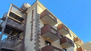 Un edificio de varios pisos con un letrero vertical llamativo, balcones con barandillas decorativas y una escalera de incendios en el lado izquierdo.