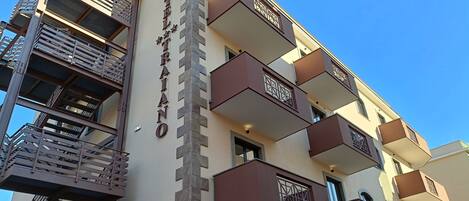 Un immeuble à plusieurs étages, doté d’une grande enseigne verticale bien visible, de balcons agrémentés de garde-corps décoratifs et d’une échelle de secours située sur le côté gauche.