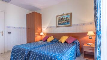 Una camera d'albergo con due letti, un armadio in legno, un comodino con una lampada e un quadro appeso al muro.