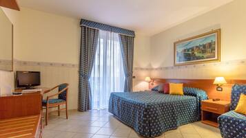 A hotel room with a bed, two bedside tables, a desk with a chair, a television, and a painting on the wall.