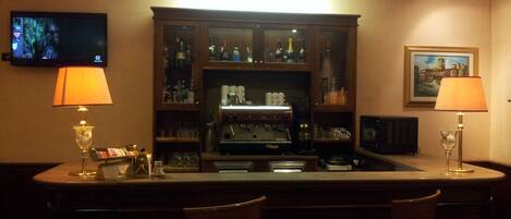 A bar area with a counter, two bar stools, a television mounted on the wall, and a cabinet with various bottles and glasses.