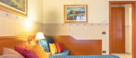 Una habitación de hotel con cabecera de madera, cama con ropa de cama estampada, mesita de noche con lámpara y un cuadro en la pared.