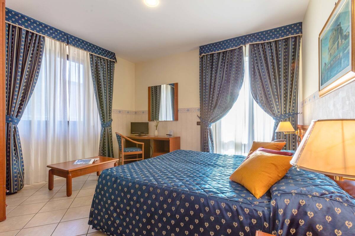 A hotel room with a bed, desk, chair, and a television.