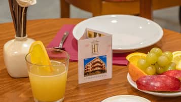 Un desayuno con vaso de zumo de naranja, taza de café, bollería y una fuente de fruta sobre una mesa de madera.