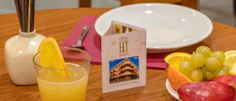 Une table en bois dressée pour le petit-déjeuner, avec un verre de jus d’orange, une tasse de café, des viennoiseries et une assiette de fruits.