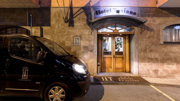 Un coche negro estacionado frente al Hotel Traiano, con una entrada de madera y un cartel sobre la puerta.